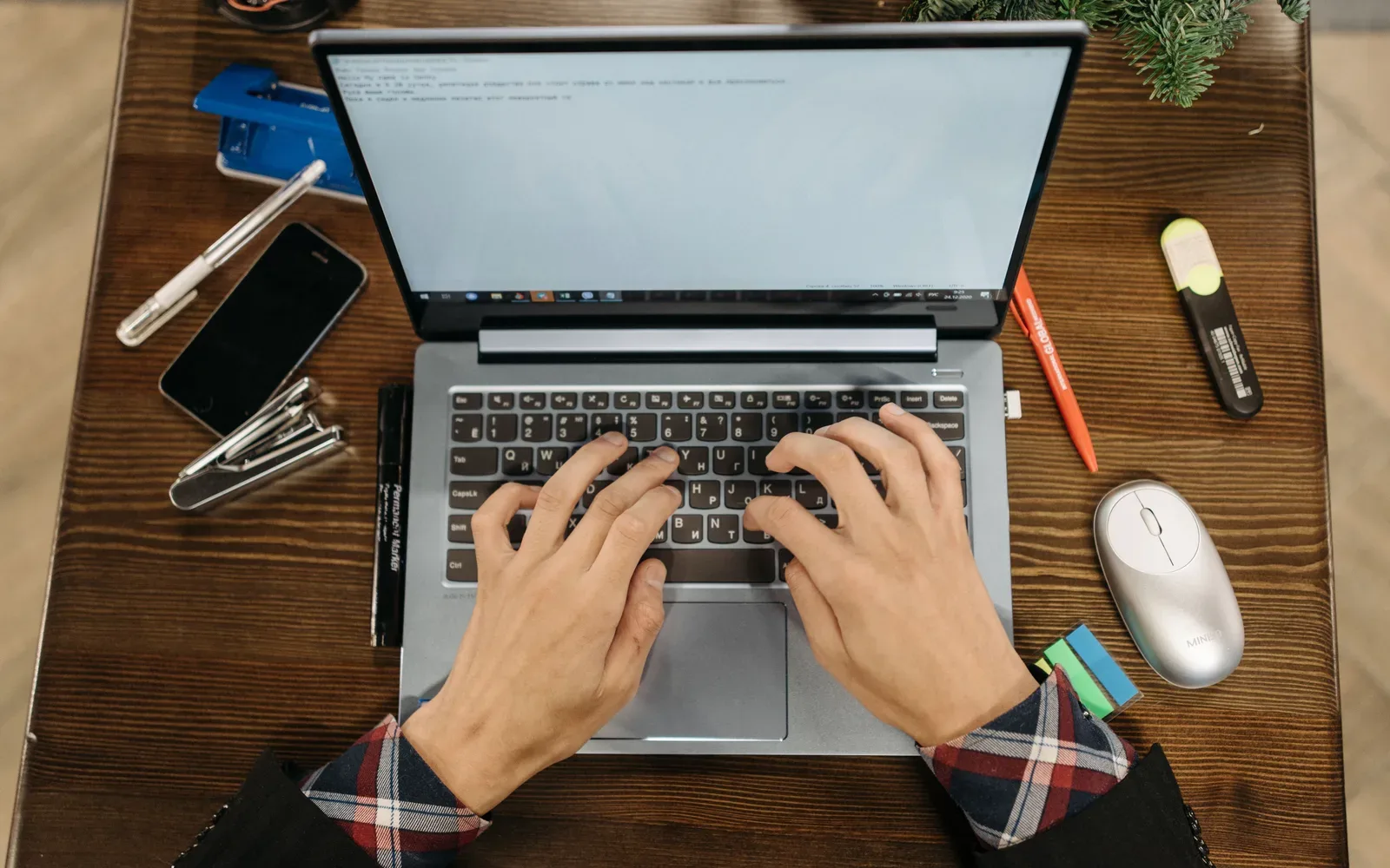 An overhead view of hands typing on a laptop on a wooden desk.