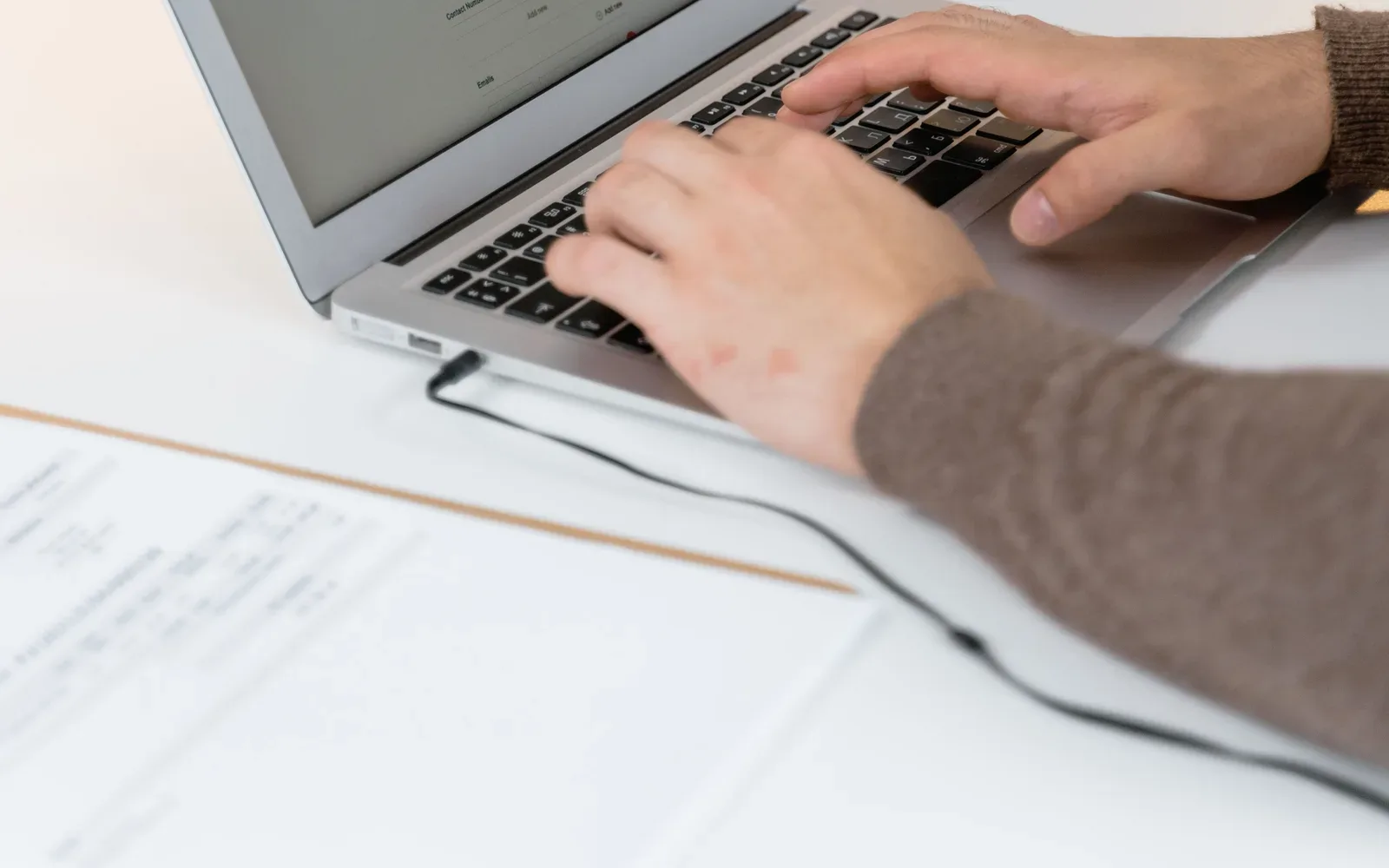 Hands typing on a laptop at a shared office table.